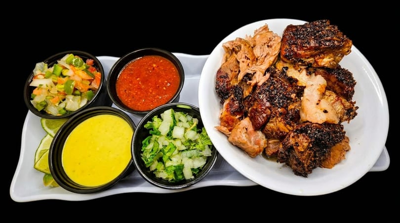 Grilled chicken pieces with four side dishes of salsa, yellow sauce, and chopped vegetables.