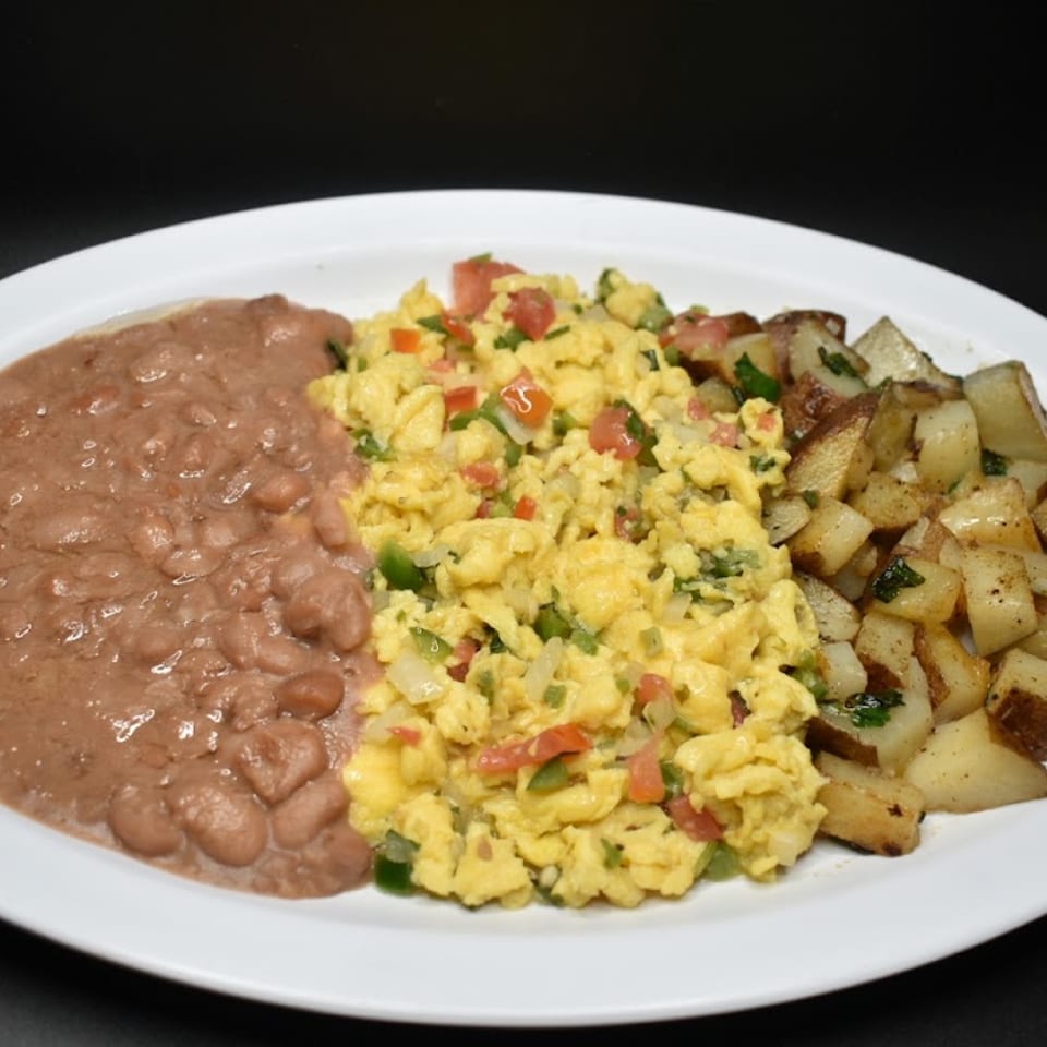 A breakfast plate with refried beans, scrambled eggs with vegetables, and roasted potatoes.