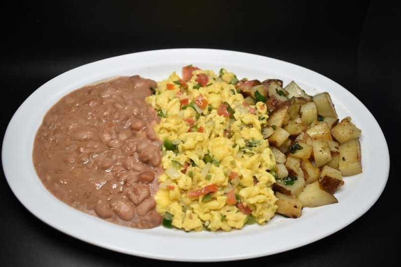 A breakfast plate with refried beans, scrambled eggs with vegetables, and roasted potatoes.